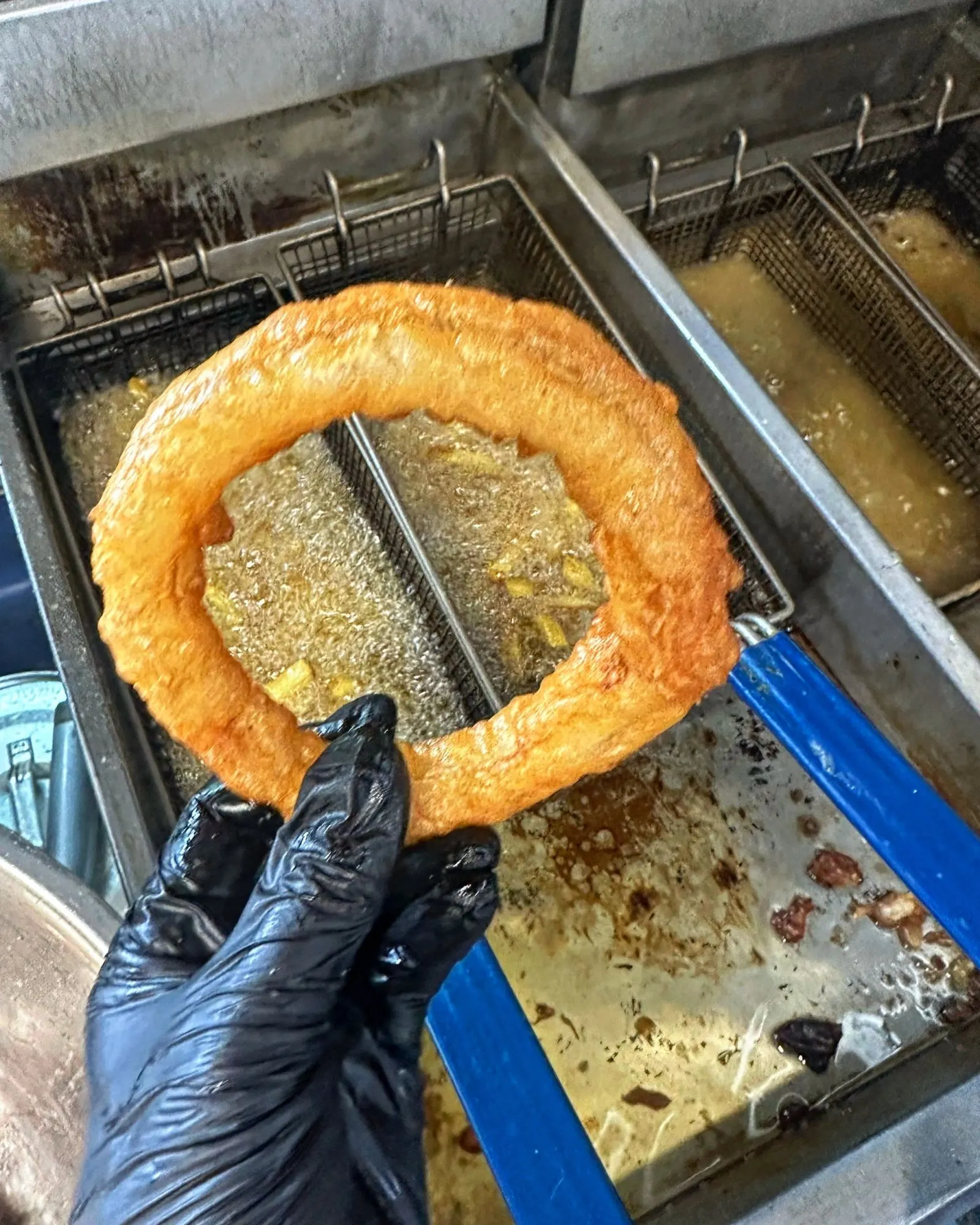 A cider-battered onion ring lifted out of the fryer