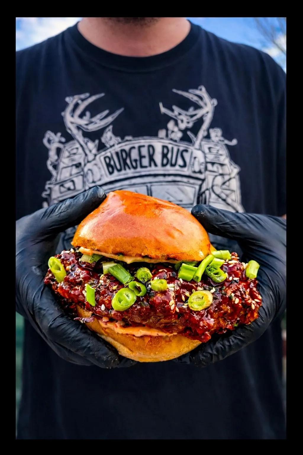 Korean fried chicken burger held up in front of a Burger Bus t-shirt